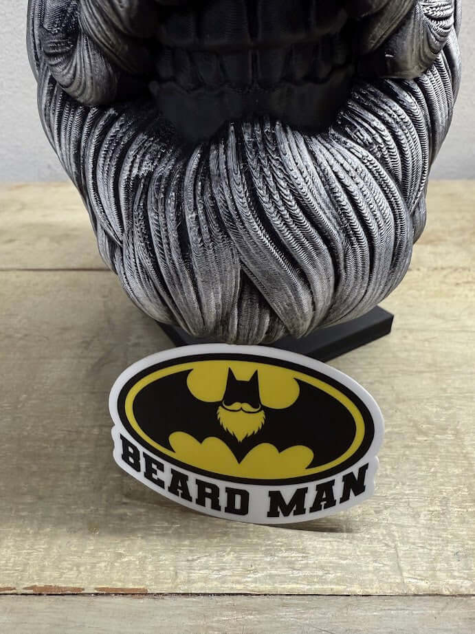 Beard Man sticker featuring a stylish bearded man in Batman logo design, placed on a textured surface.
