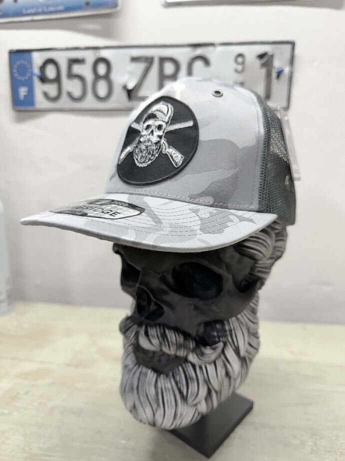 Bearded skull hunting trucker hat displayed on a skull bust, showcasing its edgy design and bold graphics.