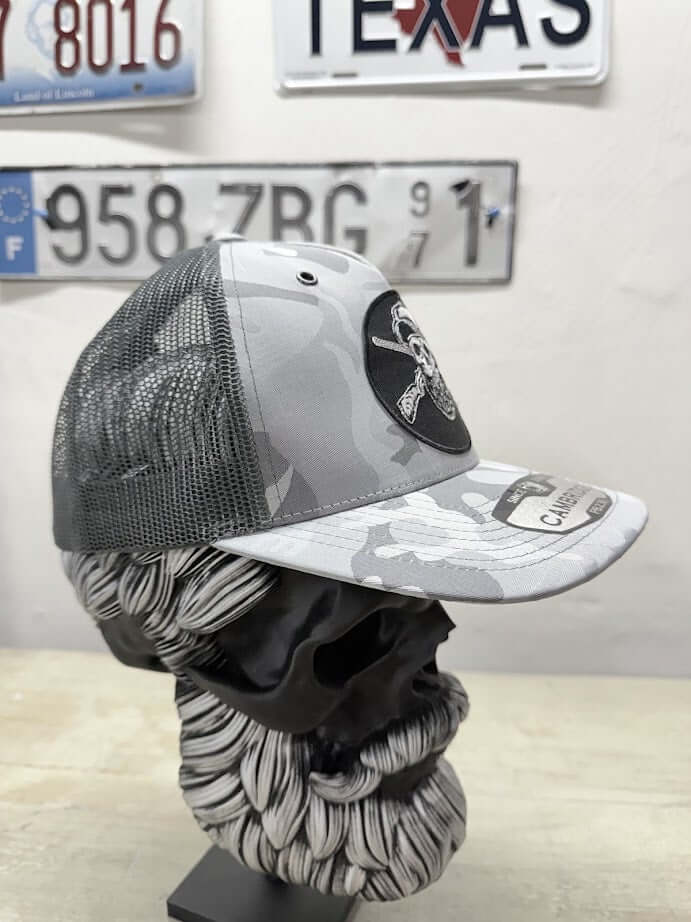 Bearded Skull Hunting Trucker Hat in gray camo displayed on a decorative bust showcasing its unique design.