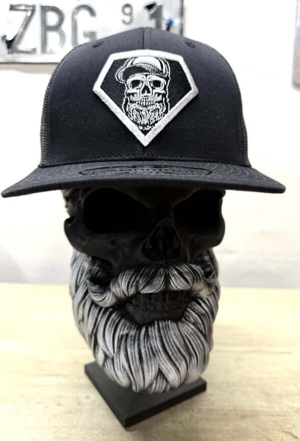 Black trucker hat with skull and beard logo displayed on a skull-shaped mannequin.