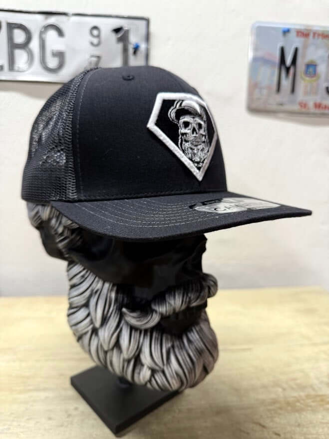 Side view of a black trucker hat with skull design on a mannequin head with a beard.
