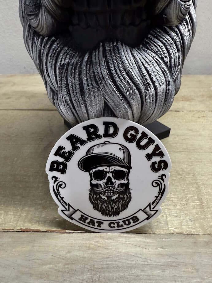 Beard Guys Hat Club logo sticker featuring a skull and beard design on a wooden table.