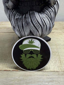 Weed Beard Man 3-Inch Sticker featuring a bearded character with cannabis design and sunglasses on a wooden table.