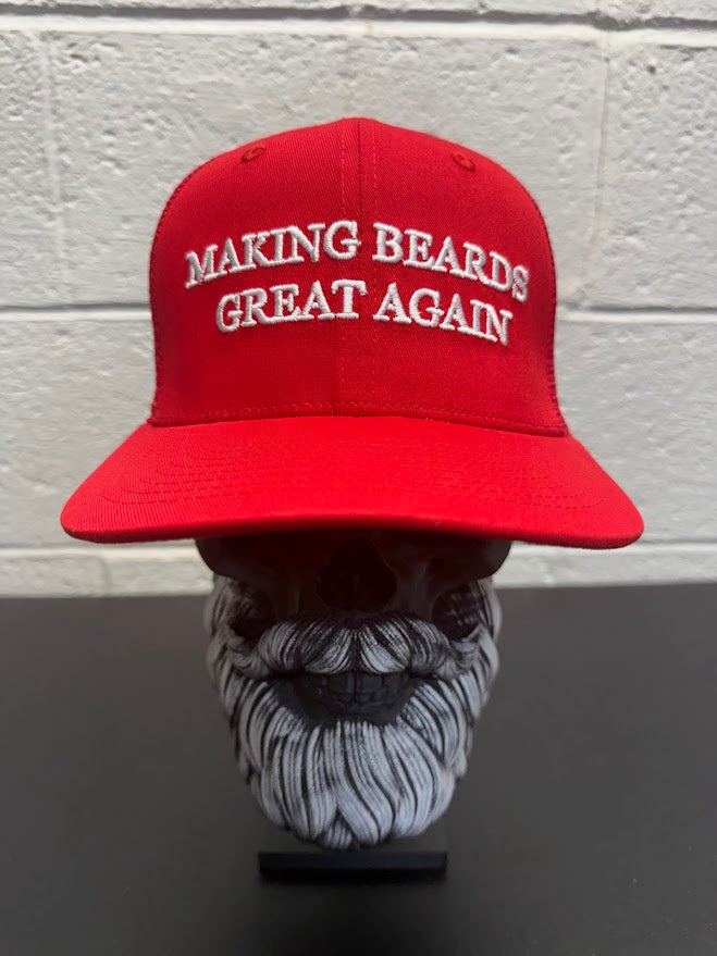 Red baseball cap with the slogan “Making Beards Great Again” displayed on a decorative beard sculpture against a neutral background.