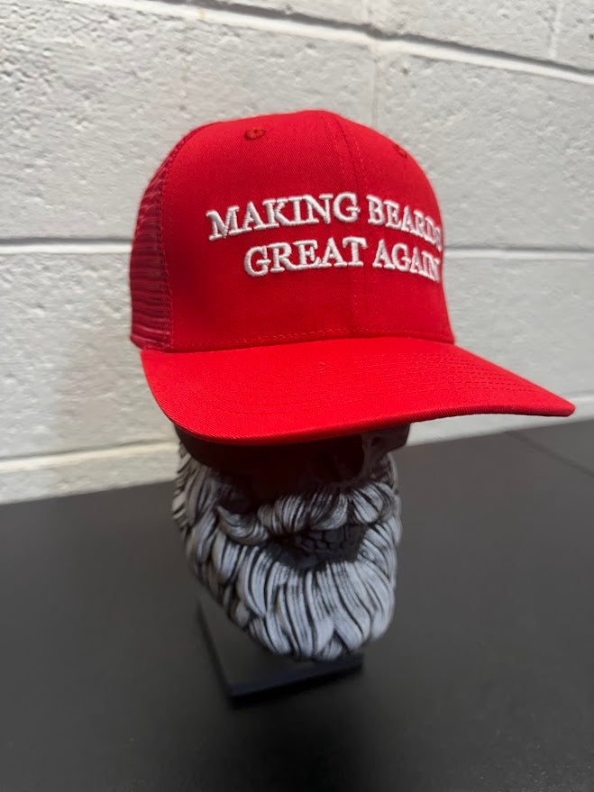 Red baseball cap with the slogan “Making Beards Great Again” displayed on a decorative beard sculpture against a neutral background.