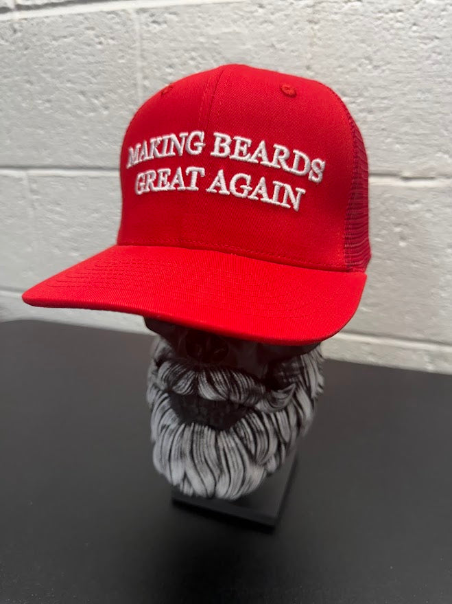 Red baseball cap with the slogan “Making Beards Great Again” displayed on a decorative beard sculpture against a neutral background.