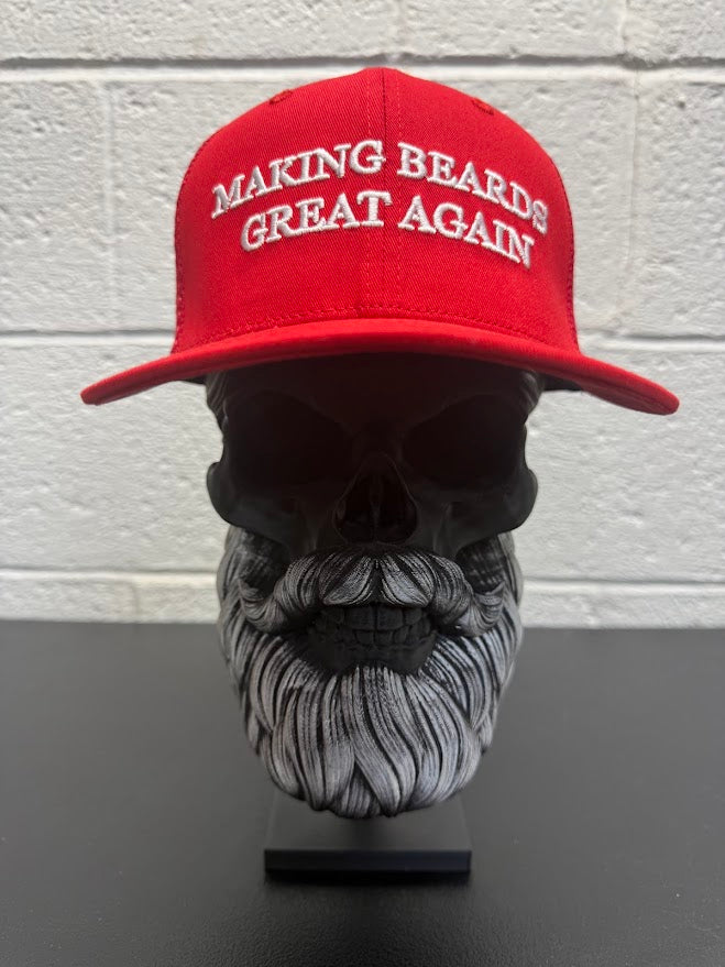 Red baseball cap with the slogan “Making Beards Great Again” displayed on a decorative beard sculpture against a neutral background.