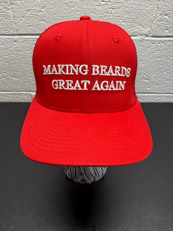 Red baseball cap with the slogan “Making Beards Great Again” displayed on a decorative beard sculpture against a neutral background.