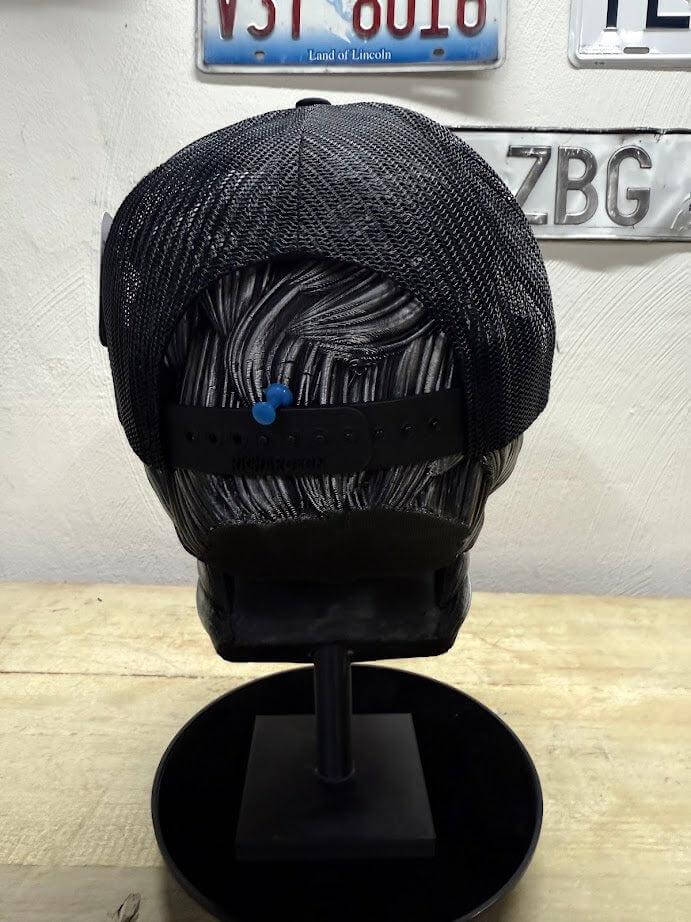 Back view of a black trucker hat with a mesh design, showcasing adjustable snap closure and unique styling.