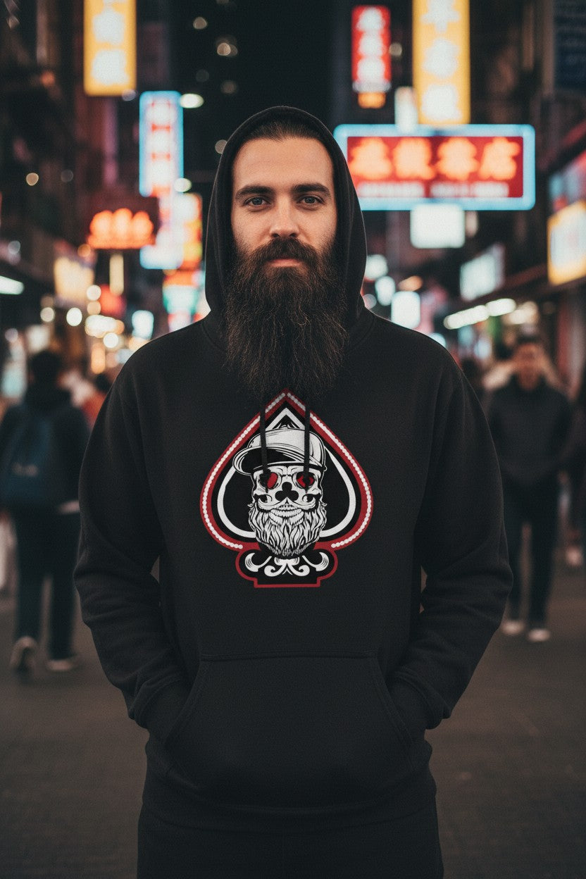 Man wearing King of Aces Bearded Skull Hoodie in a vibrant city setting with neon lights.